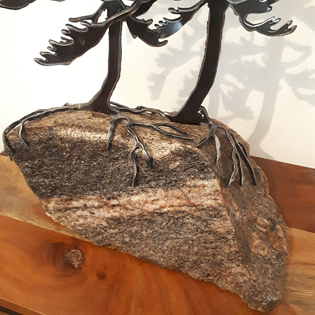 Metal sculpture of two windswept pine trees on a piece of granite
