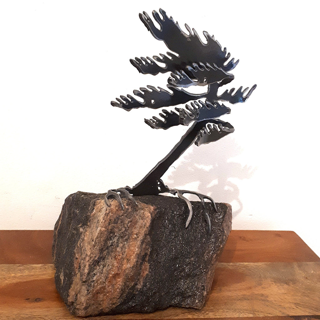 Metal sculpture of a tree with black branches on a stone base against a white background