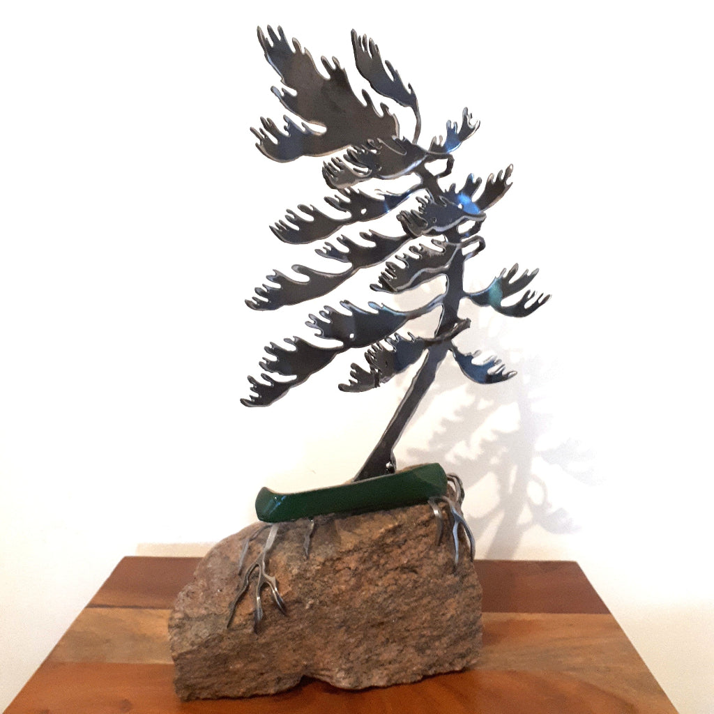 Metal tree sculpture on a rock base with a small green canoe under the tree