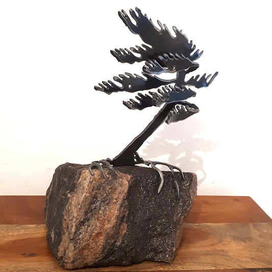 Metal sculpture of a tree with black branches on a stone base against a white background