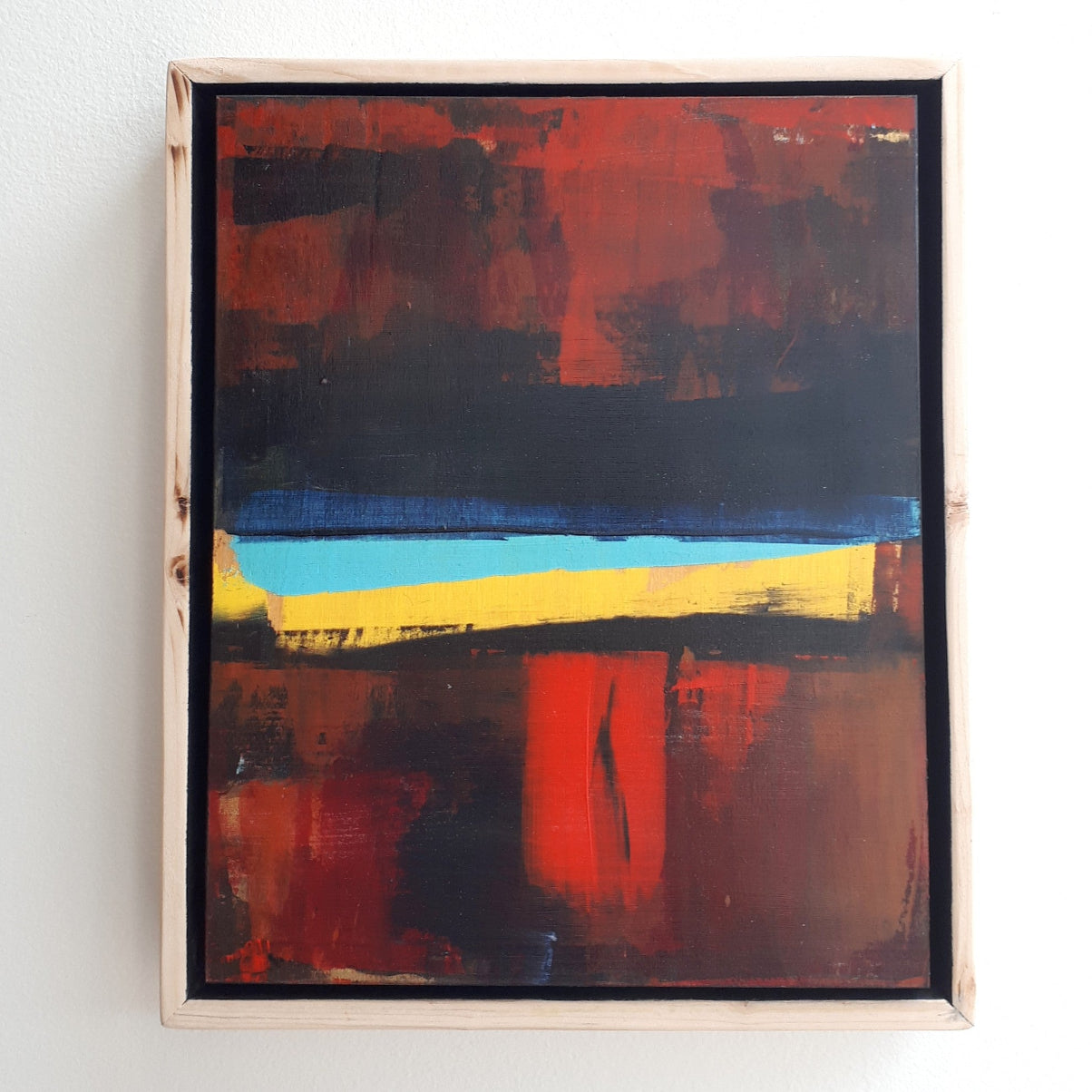 Abstract painting with red, blue, orange and yellow colors framed in a custom natural wood float frame